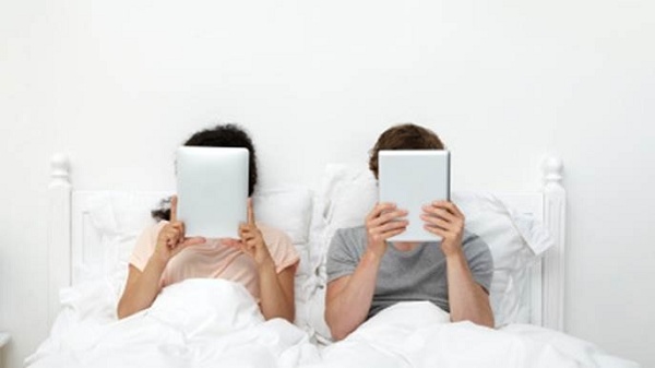 um casal usando tablets na cama